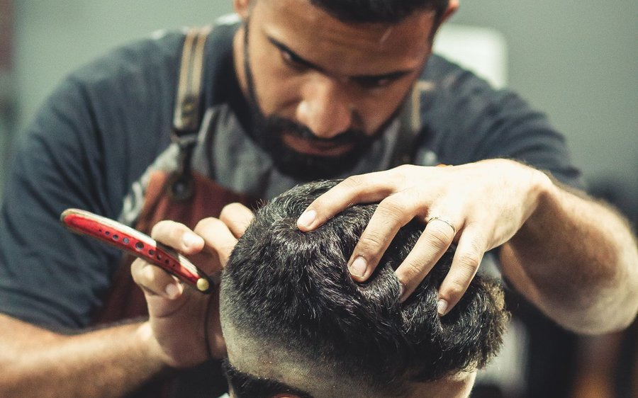 Barbershop website concept: barber trimming a client beard in a moody shot